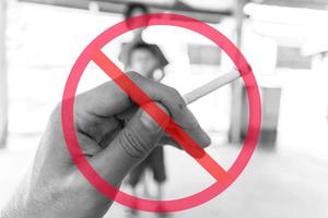 allgemeines Verbotszeichen überlagert Hand, die Zigarette mit unscharfen Kindern im Hintergrund hält