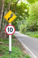 Selektive Geschwindigkeitsbegrenzung Verkehrszeichen 10 und kurvenreiches Straßenwarnsymbol für sicheres Fahren auf der Landstraße im Wald mit Bergblick, zurückhaltend foto