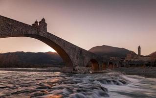 Landschaft von ein mittelalterlich Brücke Über ein turbulent Fluss beim Sonnenuntergang foto