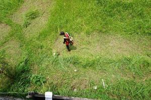 oben Aussicht von ein Mann im ein Kleid Mähen das Gras mit ein Trimmer foto