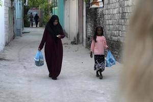 guraidhoo, malediven - märz, 4 2017 - menschen, die auf einer kleinen dorfstraße arbeiten und spazieren gehen foto