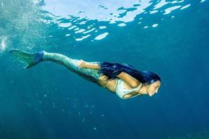 Meerjungfrau, die unter Wasser im tiefblauen Meer schwimmt foto