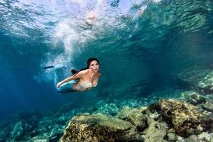 schöne meerjungfrau, die unter wasser im tiefblauen meer schwimmt foto