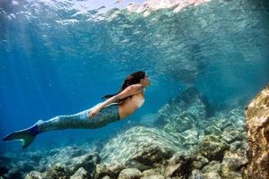 Meerjungfrau, die unter Wasser im tiefblauen Meer schwimmt foto