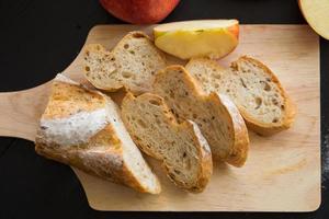 ganze und geschnittene Äpfel mit geschnittenem Baguette auf Holzbrett auf einem dunklen Holztisch foto