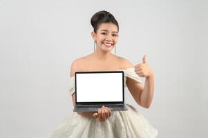 junge asiatische schöne brauthaltung mit mockup-laptop-computer in der hand foto