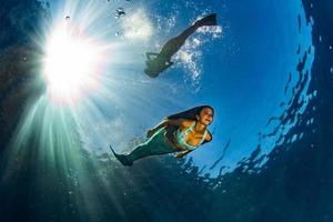 zwei Meerjungfrauen schwimmen unter Wasser im tiefblauen Meer foto