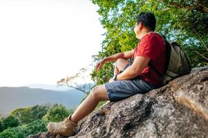 junger Rucksacktourist, der mit Rucksack auf felsigen Klippen sitzt foto