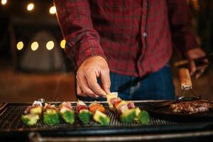 Nahaufnahme der Hand des Mannes, der auf der Neujahrsparty Fleisch auf dem Grill kocht. bar-bq oder bbq auf traditionellem herd. nachtparty, menschen und feierkonzept. foto