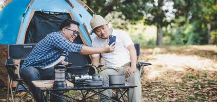 porträt glückliche asiatische mannfreunde, die einen videoanruf mit smartphone beim camping machen foto