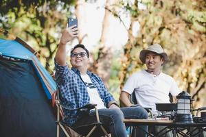 porträt glückliche asiatische mannfreunde, die einen videoanruf mit smartphone beim camping machen foto