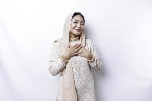 glücklich achtsam dankbar jung asiatisch Muslim Frau mit ihr Hand auf ihr Truhe lächelnd isoliert auf Weiß Hintergrund foto