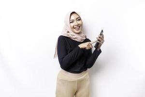 ein Porträt von ein glücklich asiatisch Muslim Frau tragen ein Kopftuch, halten ihr Telefon, isoliert durch Weiß Hintergrund foto