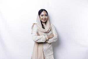 Porträt von ein zuversichtlich lächelnd asiatisch Muslim Frau tragen Hijab Stehen mit Waffen gefaltet und suchen beim das Kamera isoliert Über Weiß Hintergrund foto