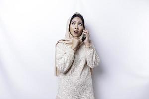 schockiert asiatisch Frau tragen Kopftuch, halten ihr Telefon, isoliert durch Weiß Hintergrund foto
