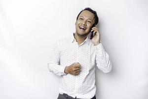 aufgeregt asiatisch Mann tragen Weiß Hemd lächelnd während halten seine Telefon, isoliert durch Weiß Hintergrund foto