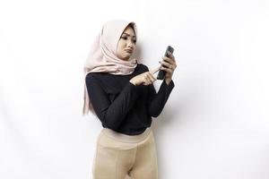 ein unzufrieden jung asiatisch Muslim Frau sieht aus verärgert tragen Hijab gereizt Gesicht Ausdrücke halten ihr Telefon foto