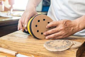 Zimmermann anfügen Sandpapier zu ein Orbital Schleifer oder Palme Schleifer nach entfernen das Papier Rückendeckung von das Schleifpapier.diy Hersteller und Holzbearbeitung Konzept. selektiv Fokus foto