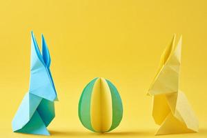 zwei Origami-Esater-Kaninchen aus Papier und farbiges Ei auf gelbem Hintergrund foto