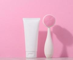 Weiß Plastik Tube und ein Massage Bürste zum Gesichts- Reinigung auf ein Rosa Hintergrund, Artikel zum kosmetisch Verfahren foto