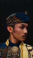 ein asiatisch Mann tragen ein traditionell Kostüm mit schön Motive auf seine Hemd und tragen ein Bandana namens ein Bendo im ein Zimmer foto