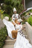 ein Paar von Bräute im Weiß Kleider wurden Sitzung auf das Treppe mit ein heiter Gesichter und voll von Zuneigung im das Mitte von das Garten foto