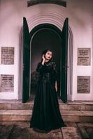 ein Hexe im ein alle schwarz Kleid und unheimlich bilden war Stehen beim das Friedhof Tor foto