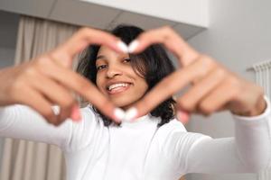 Foto Porträt von Frau Herstellung Herz mit Hände in der Nähe von Auge suchen durch beim heim. Liebe, Romantik, Valentinstag Tag Konzept