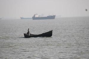 Angeln Boot auf das sehen Küste mit Ladung Schiff auf das Hintergrund foto