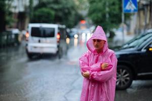 traurige Frau in einem Regenmantel auf der Straße im Regen foto