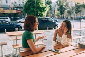 Zwei hübsche Freundinnen unterhalten sich, während sie im Freien in einer Bar sitzen foto