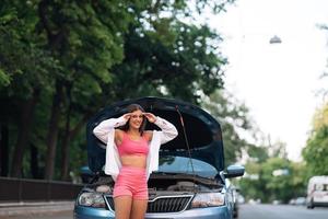 Frau mit kaputtem Auto auf der Straße. Hilfe suchen. foto