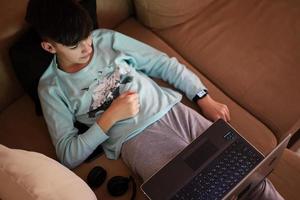 jung Teen Junge im Vorderseite von ein Laptop auf ein Bett beim Abend. foto