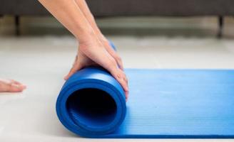 Yoga beim heim. jung Lebensstil Frau rollen Blau Matte auf Fußboden nach ein trainieren im Leben Zimmer foto