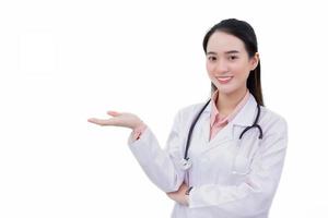 Fachmann asiatisch Frau Arzt trägt medizinisch Mantel während Stehen selbstbewusst lächelnd und zeigt an ihr Hand zu Geschenk etwas isoliert auf Weiß Hintergrund im Gesundheit Schutz Konzept. foto