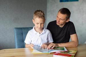 ein süß Junge ist Sitzung beim das Tabelle mit seine Papa und Aufpassen ein Buch Über Schlangen foto