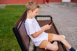 das Junge ist Sitzung auf ein Bank und suchen beim das Telefon foto