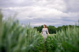 ein süß Mädchen mit lange Haar im ein Kleid läuft durch ein Weizen Feld foto