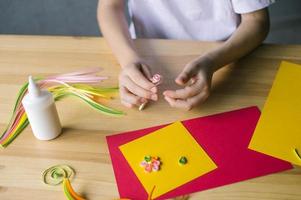 mit das Hände von ein Kind, machen ein Karte aus von Quilling, Twist ein Streifen von Rosa Papier mit ein Ahle foto