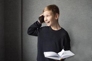 ein glücklich Junge ist halten ein Buch im seine Hände und reden auf das Telefon foto