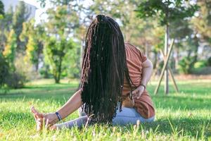 schön jung Frau mit lange afrikanisch Zöpfe ist tun Yoga draußen im ein Park. Konzept von gesund Lebensstil. foto