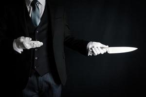 Porträt von Diener im dunkel passen und Weiß Handschuhe halten Scharf Messer. Konzept von Diener tat Es. foto