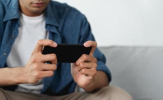 Mann verwenden Smartphone auf Sofa im Leben Zimmer beim heim, spielen Handy, Mobiltelefon Spiele, Video streamen, suchen Daten, und Sozial Medien auf Internet. foto