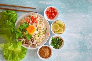 sofortig Nudeln Kochen lecker Essen mit Platte, Nudeln Schüssel mit gekocht Ei gehackt Schweinefleisch Gemüse Frühling Zwiebel Zitrone Limette Grüner Salat Sellerie und Chili auf Tabelle Essen, Nudel Suppe foto