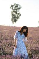 Porträt von ein glücklich Frau im ein Blau Kleid genießen ein sonnig Sommer- Tag im ein Lavendel Feld. frisch Luft, Lebensstil. foto