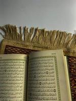 lesen al Koran und drehen Seite von Koran über Sajada beten Matte isoliert auf Weiß Raum. ausgewählt Fokus foto