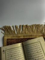lesen al Koran und drehen Seite von Koran über Sajada beten Matte isoliert auf Weiß Raum. ausgewählt Fokus foto