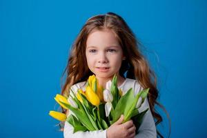 Porträt von ein charmant lächelnd wenig Mädchen mit ein Strauß von Tulpen im ihr Hände. Lebensstil. frisch Blumen. International Damen Tag. Raum zum Text. hoch Qualität Foto