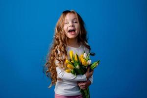 Porträt von ein charmant lächelnd wenig Mädchen mit ein Strauß von Tulpen im ihr Hände. Lebensstil. frisch Blumen. International Damen Tag. Raum zum Text. hoch Qualität Foto