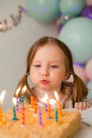 süß wenig Mädchen weht aus Kerzen auf ein Geburtstag Kuchen beim Zuhause gegen ein Hintergrund von Luftballons. Kinder Geburtstag foto